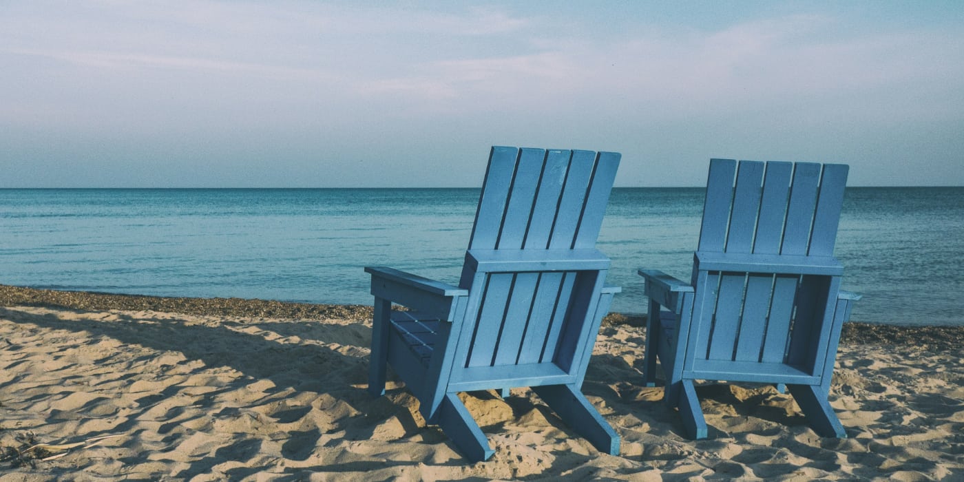 Two empty chairs on a sandy beach overlooking water